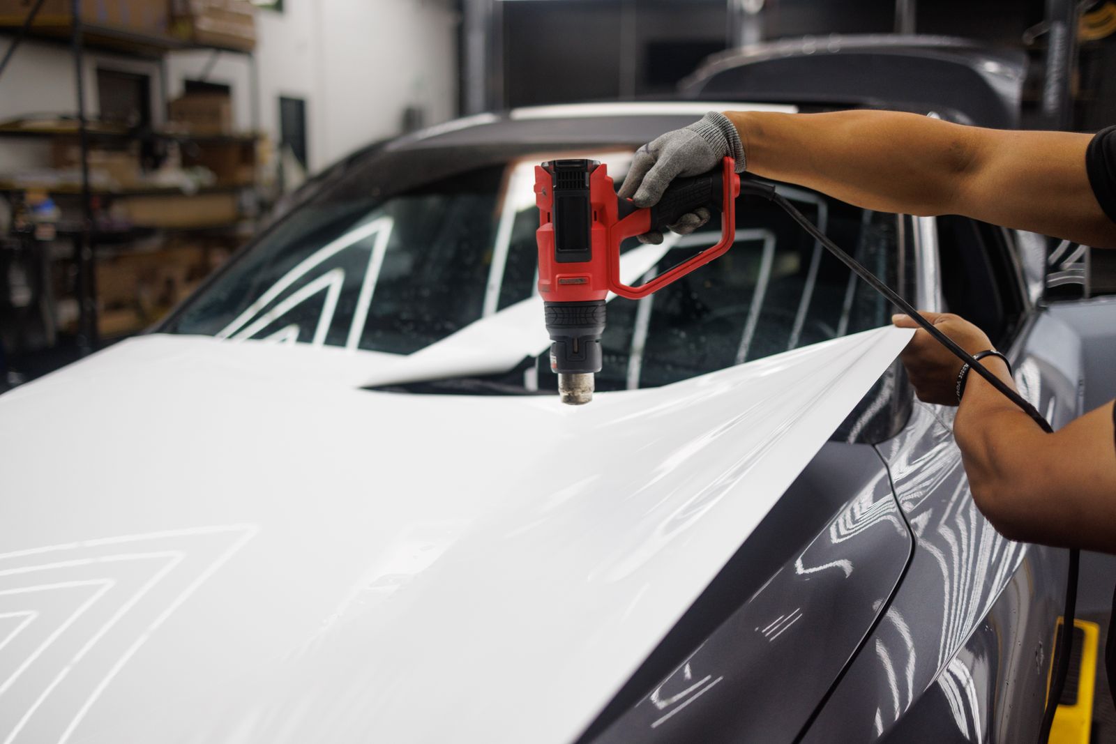 Installer fitting paint protection film to a car with a heat gun