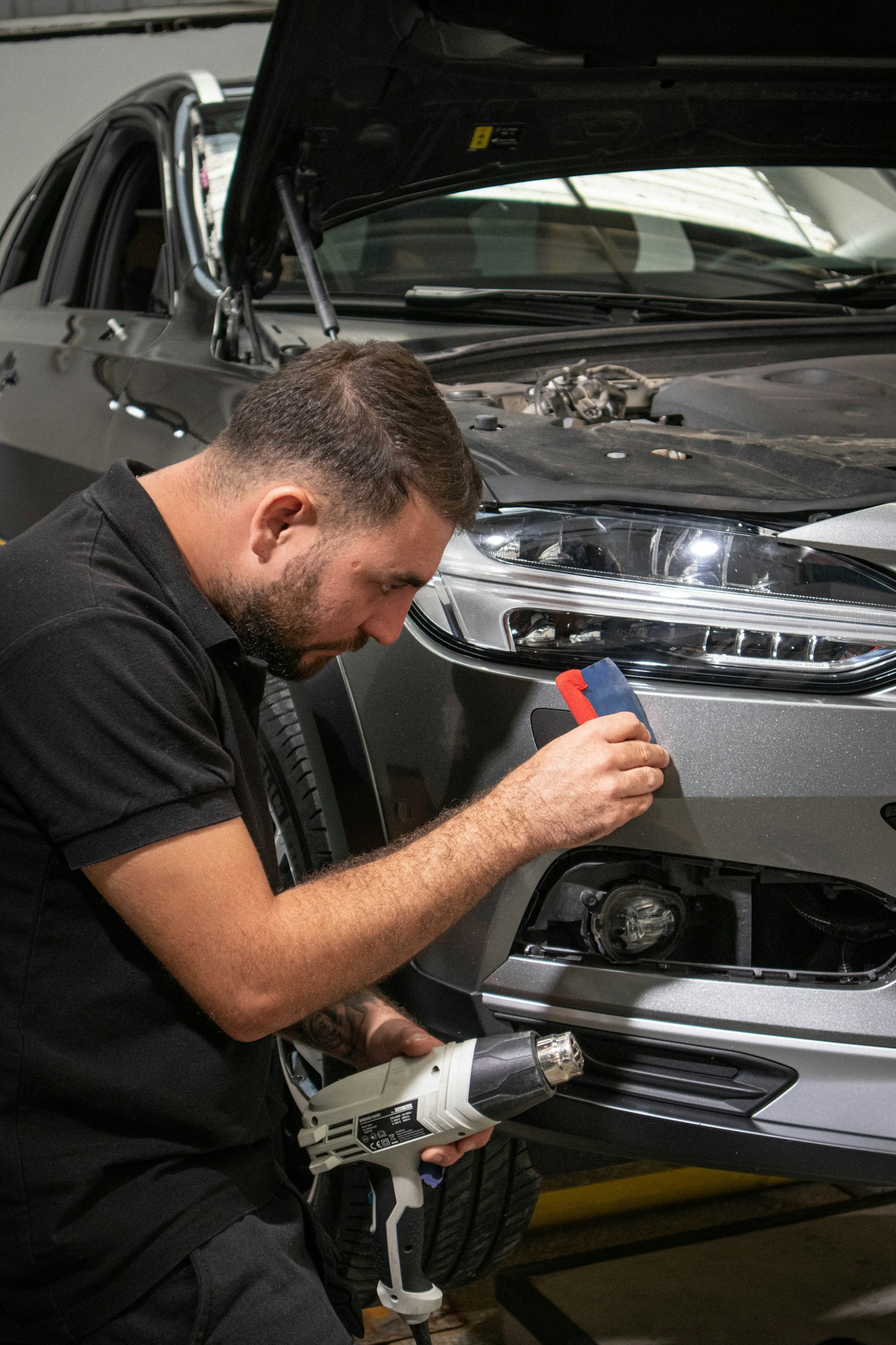 Installer fitting paint protection film around a headlight