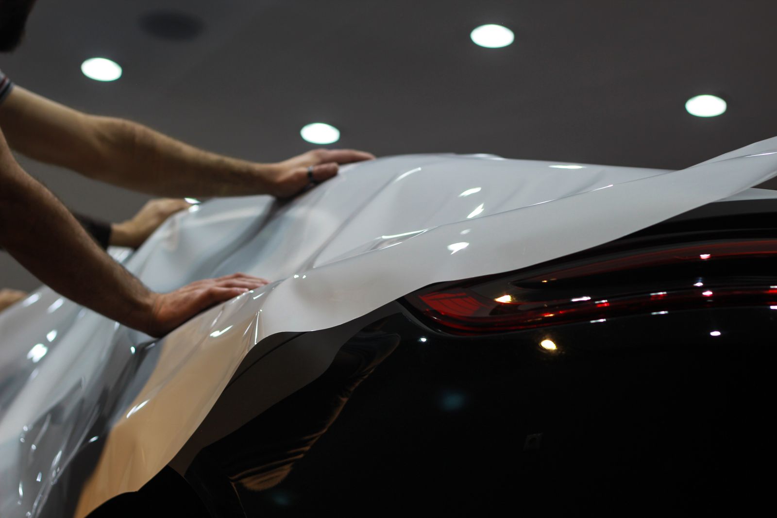 Installer laying a sheet of gloss film across a car